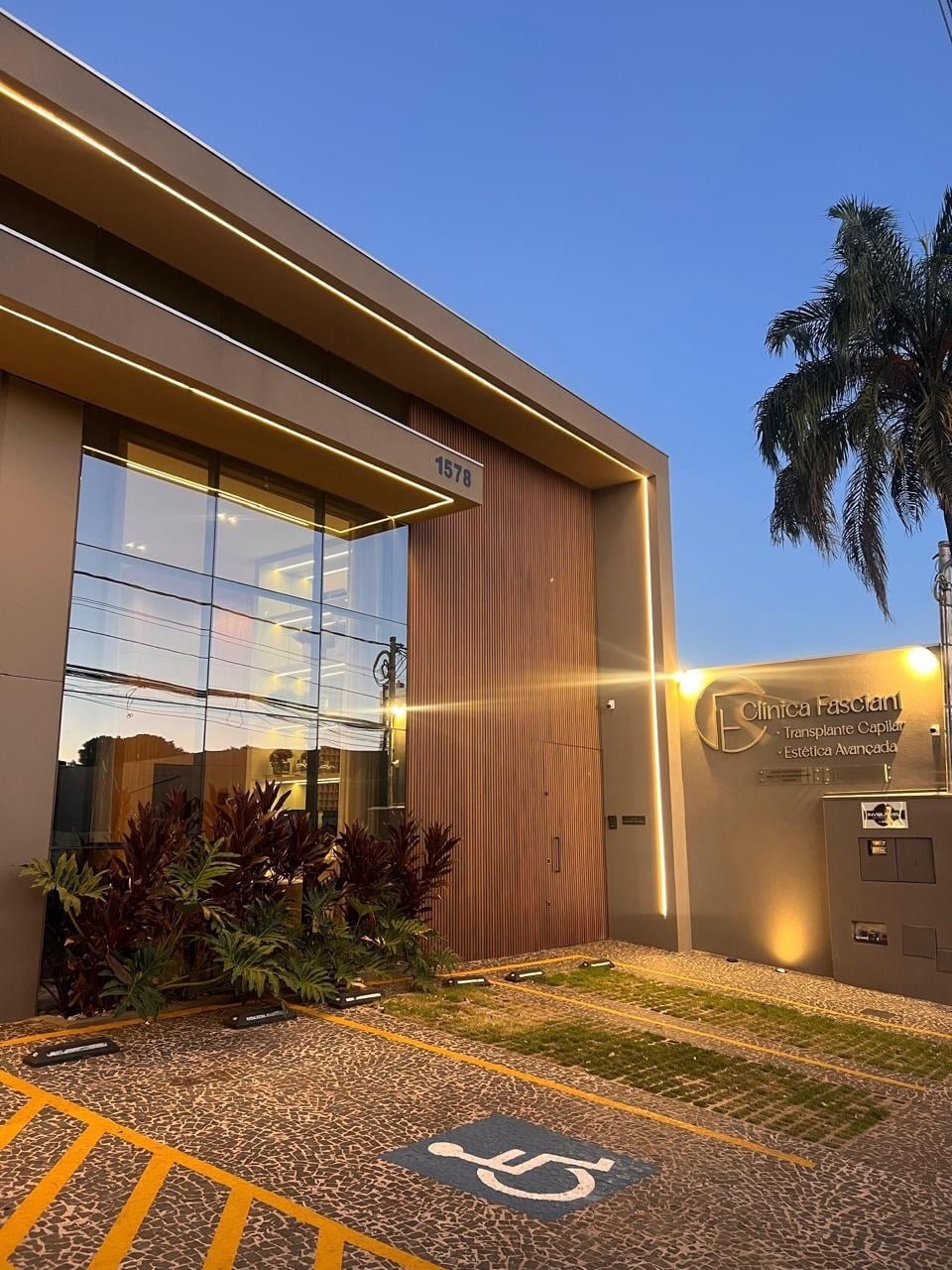 Entrada da clínica com jardim de plantas vermelhas, vidro alto e ripado de madeira