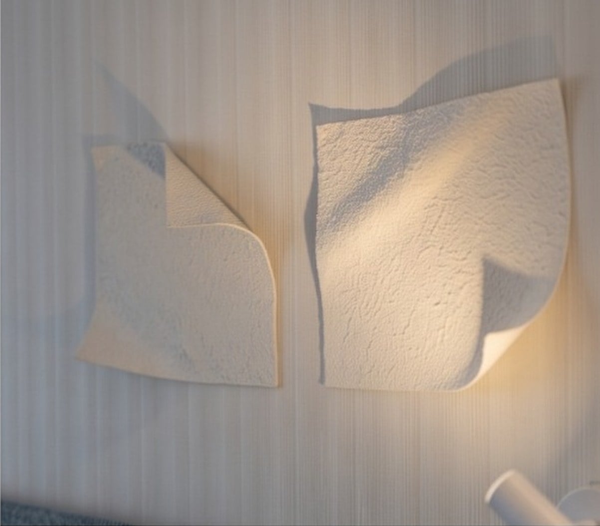 Esculturas de papel em relevo na parede clara, iluminadas de lado