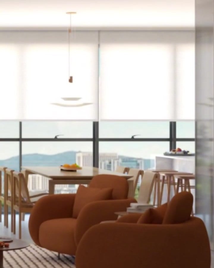 Sala com poltronas laranja diante de janelas amplas com vista para o mar